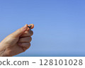 Close up of hand holding shark tooth against sandy Gulf coast background with sea horizon 128101028