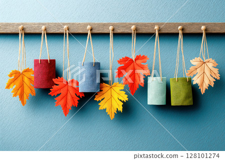 Small textile gift bags and bright autumn leaves hanging on wooden hooks against a blue wall 128101274