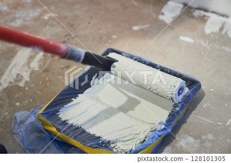 Apartment renovation. Concrete walls are painted gray with a paint roller. A container of paint for a paint roller. High quality photo 128101305