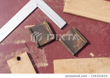 Woodworking elements arranged on a reddish surface. Two dark grooved blocks, two screws, a carpenter square, and light wood pieces Woodworking elements arranged on a reddish surface. Two dark grooved blocks, two screws, a carpenter square, and light wood pieces 128101619