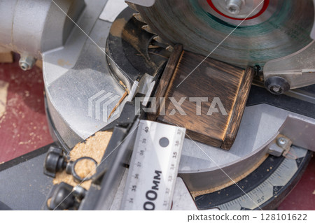 A close-up of a miter saw actively cutting through wood, with a cloud of sawdust around the blade. A close-up of a miter saw actively cutting through wood, with a cloud of sawdust around the blade. 128101622