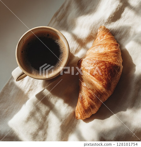 A delicious breakfast featuring a fresh croissant and a hot cup of coffee. 128101754