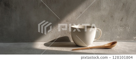 A serene still life featuring a ceramic mug and wooden spoon on concrete. 128101804