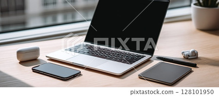 Modern workspace with a laptop, smartphone, and wireless earbuds. 128101950