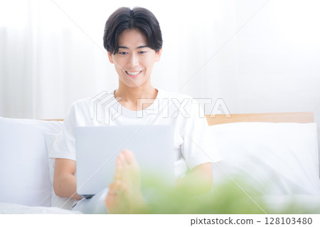 A man using a computer in bed, front view of a freelancer or busy office worker 128103480