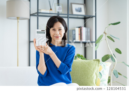 A middle-aged woman looking at a calculator in the living room A middle-aged woman looking at a calculator in the living room 128104531