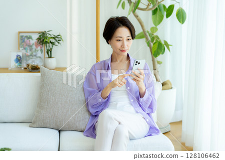 Middle-aged woman using a smartphone in a room Middle-aged woman using a smartphone in a room 128106462