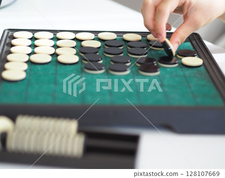 Child's hand flipping an Othello stone and the board 128107669