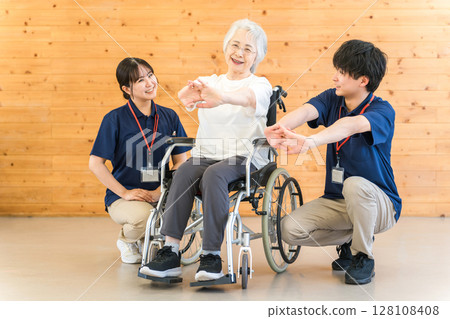 一名坐在輪椅上的老年婦女在復健期間做體操，以及男女物理和職業治療師人員 128108408