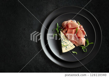 Blue cheese, prosciutto, and rosemary on a black table. 128110340