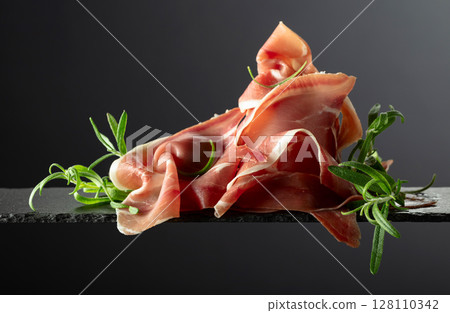 Prosciutto with rosemary on a black background. 128110342