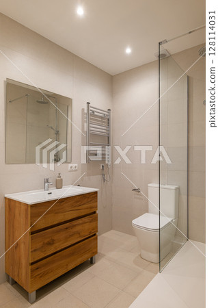 Bathroom with beige tiled walls, wood vanity with white sink, glass shower and chrome fixtures 128114031
