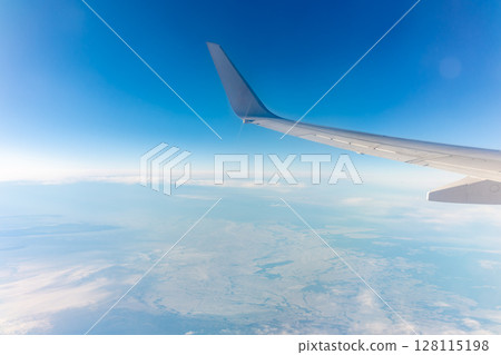 View from the airplane window at a beautiful blue clear sky, earth, sea and the airplane wing View from the airplane window at a beautiful blue clear sky, earth, sea and the airplane wing 128115198