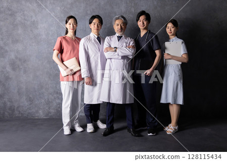 A team of medical workers standing in front of a black wall A team of medical workers standing in front of a black wall 128115434