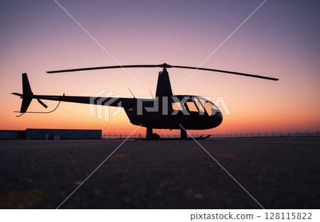 A black helicopter is sitting on the ground at sunset. A black helicopter is sitting on the ground at sunset. 128115822