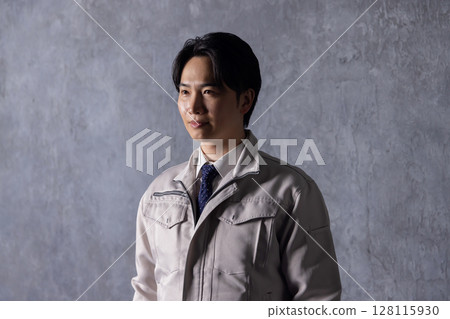 A man in work clothes standing in front of a black wall A man in work clothes standing in front of a black wall 128115930