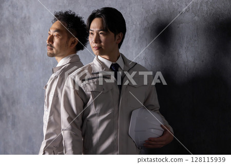 一位身穿工作服的男子微笑著站在黑牆前 128115939