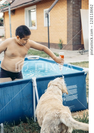 boy playing with water in outdoor pool pouring water from bottle for wet labrador dog to drink summer backyard near brick house concept of pet care animal health outdoor recreation boy playing with water in outdoor pool pouring water from bottle for wet labrador dog to drink summer backyard near brick house concept of pet care animal health outdoor recreation 128118662