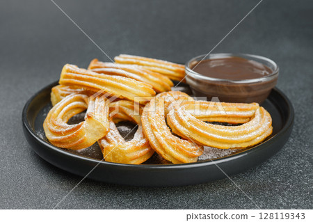 Traditional spanish dessert churros, fried dough pastry and chocolate sause on black background 128119343