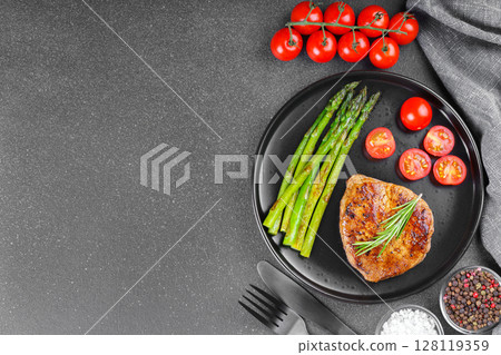 Grilled beef steak with asparagus and cherry tomatoes on black plate on gray background, copy space Grilled beef steak with asparagus and cherry tomatoes on black plate on gray background, copy space 128119359