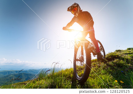 Cyclist man on mountain bike outdoors. Male tourist riding bicycle on grassy trail in mountains wearing helmet and protective glasses. Sport, outdoor activities and nature concept Cyclist man on mountain bike outdoors. Male tourist riding bicycle on grassy trail in mountains wearing helmet and protective glasses. Sport, outdoor activities and nature concept 128120525