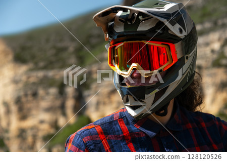Close-up portrait of young sportsman wearing protective helmet and protective mask on his face. Mature guy resting looking at camera after hard training in mountains 128120526