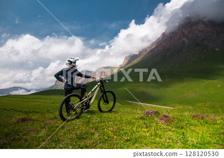 Male athlete cyclist in helmet and protective mask outdoors. MTB rider in mountainous terrain against the backdrop of epic rocks. Male athlete cyclist in helmet and protective mask outdoors. MTB rider in mountainous terrain against the backdrop of epic rocks. 128120530