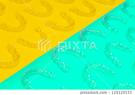 Invisible orthodontic cosmetic aligners on a colored background, aligners, plastic braces. Modern dental retainers created on a 3D printer 128120533