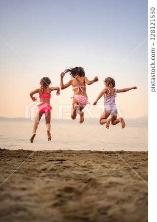 Joyful children leap into the air at a serene beach sunset Joyful children leap into the air at a serene beach sunset 128121530