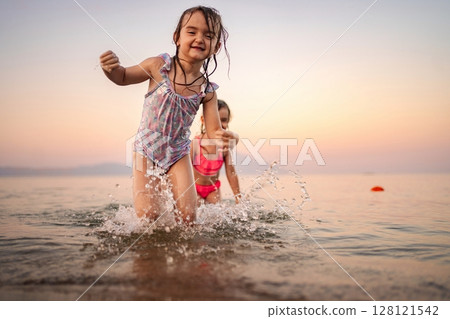 Joyful children playing in the gentle waves at sunset by the shore 128121542