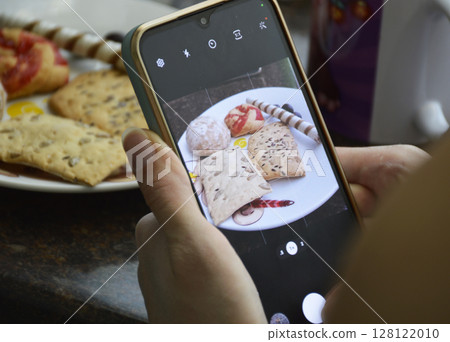 female hands holding smartphone and taking photo of sweet food 128122010