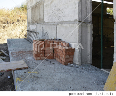 stacks of red bricks near the wall of an unfinished house 128122014