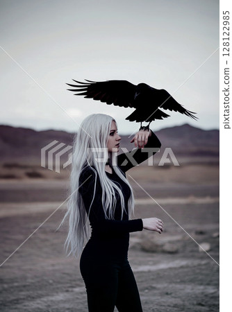 一位白髮女子站在荒原上，手臂上停著一隻烏鴉 128122985