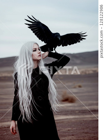 A grey-haired woman standing in a wasteland with a crow on her arm A grey-haired woman standing in a wasteland with a crow on her arm 128122986