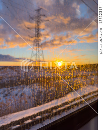 Sunset view from a train window with raindrops against the glass in a snowy landscape Sunset view from a train window with raindrops against the glass in a snowy landscape 128123184