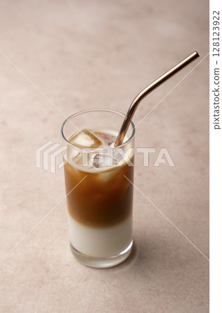 Coffee with coconut milk and ice cubes in a tall glass. Traditional non-alcoholic cold drink. In the background, a jar of coffee and a jar of sugar. Selective focus, close-up. Coffee with coconut milk and ice cubes in a tall glass. Traditional non-alcoholic cold drink. In the background, a jar of coffee and a jar of sugar. Selective focus, close-up. 128123922