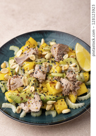 Salad with canned tuna, peanuts, mango, avocado, celery, chili flakes and black sesame. Light summer salad with olive oil and a lemon lobule. Home cooking. Selective focus, close-up. Salad with canned tuna, peanuts, mango, avocado, celery, chili flakes and black sesame. Light summer salad with olive oil and a lemon lobule. Home cooking. Selective focus, close-up. 128123923