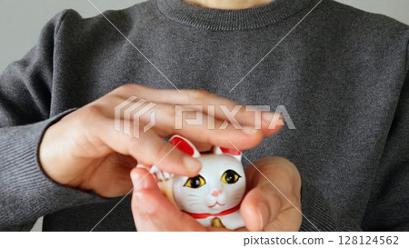 A person stroking the head of a maneki-neko 128124562