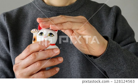 A person stroking the head of a maneki-neko 128124563