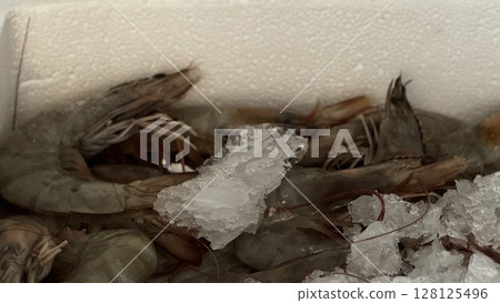 Fresh raw shrimp laid out on crushed ice in a market crate, ideal for culinary, seafood, or sustainable fishing themes. 128125496
