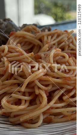 A tight close-up of freshly prepared spaghetti with tomato sauce, ideal for food blogs, recipes, or Mediterranean dining visuals. A tight close-up of freshly prepared spaghetti with tomato sauce, ideal for food blogs, recipes, or Mediterranean dining visuals. 128125499