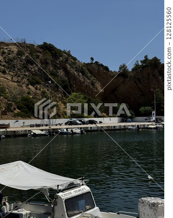 Small white fishing boats floating in a calm coastal harbor with rocky cliffs in the background ideal for travel and lifestyle content. 128125560
