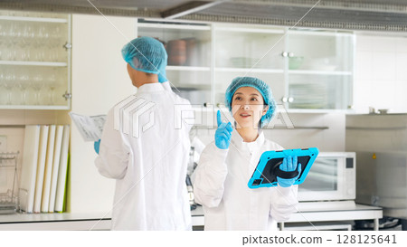 Male and female workers in sanitary white coats checking the kitchen 128125641
