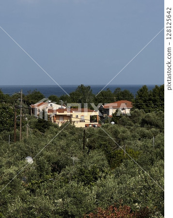 Scenic view of village homes nestled in dense greenery with a glimpse of sea in background, ideal for travel and nature visuals. 128125642