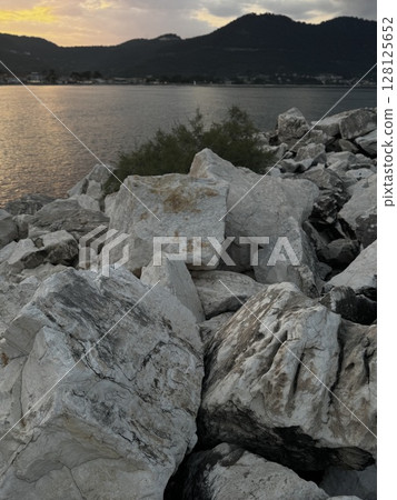 Large white rocks along a calm shoreline during sunset, reflecting warm tones, perfect for nature, travel, and tranquil seascapes. Large white rocks along a calm shoreline during sunset, reflecting warm tones, perfect for nature, travel, and tranquil seascapes. 128125652