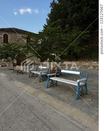 Traditional blue-painted benches on a quiet stone street in a Greek island village, ideal for travel and architecture themes. 128125667