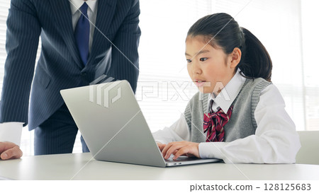A girl learning how to use a computer from a male teacher in a classroom 128125683