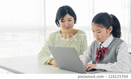 一名女孩在教室裡向女老師學習如何使用電腦 128125709