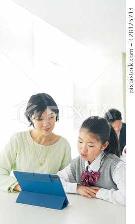 一位女老師正在指導一位女孩使用平板電腦 128125713