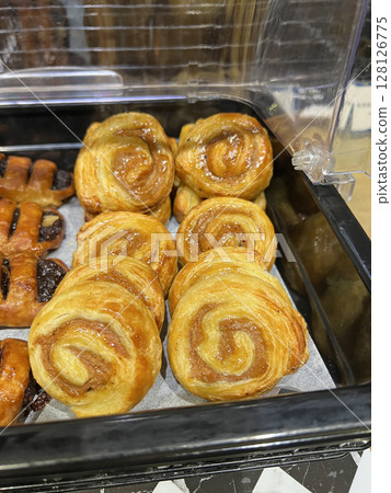Photographing neatly arranged cinnamon rolls and chocolate danishes in a cafeteria 128126775